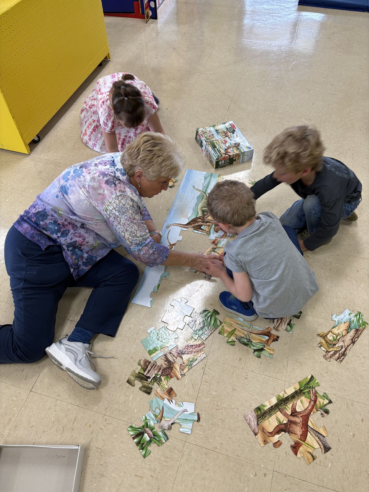 Teacher helping students assemble a dinosaur puzzle on the floor at Noah's Ark Preschool